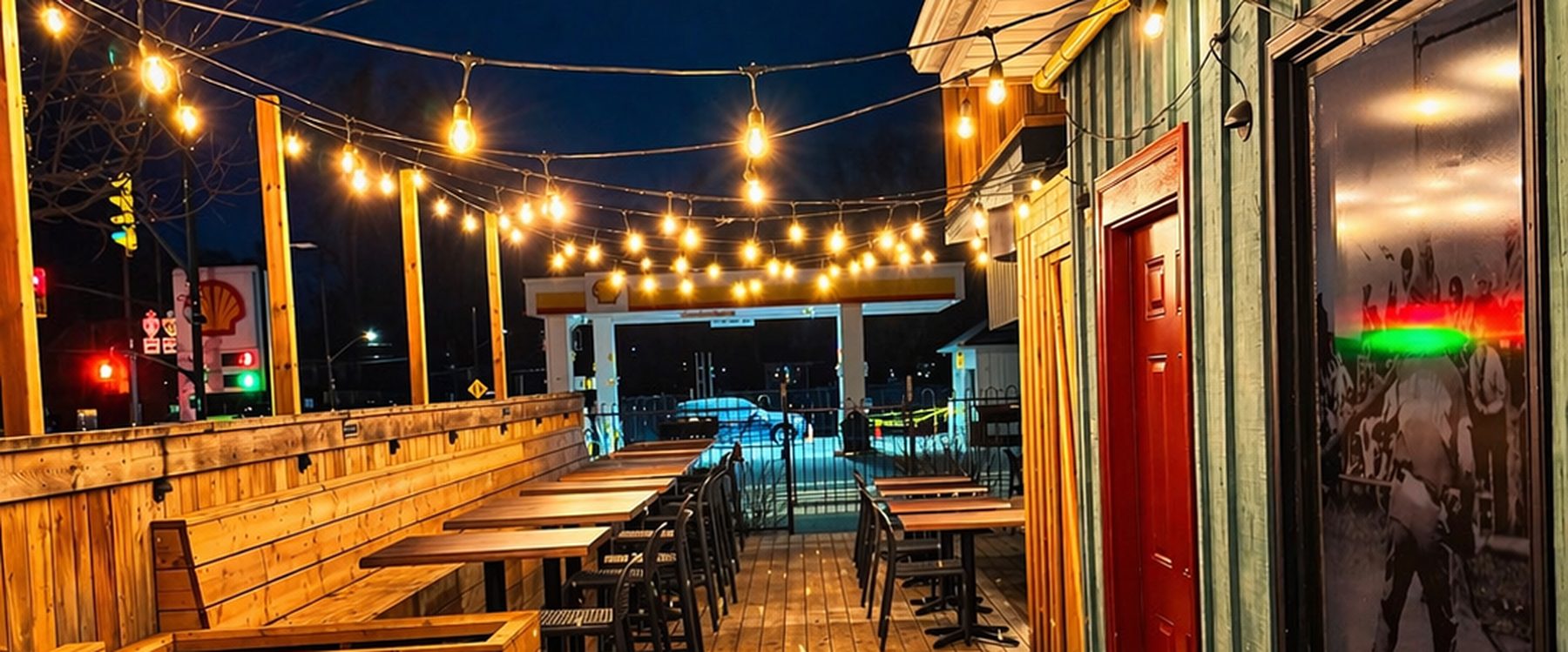 String lights over the Backroads patio at night, wooden tables and benches along the deck